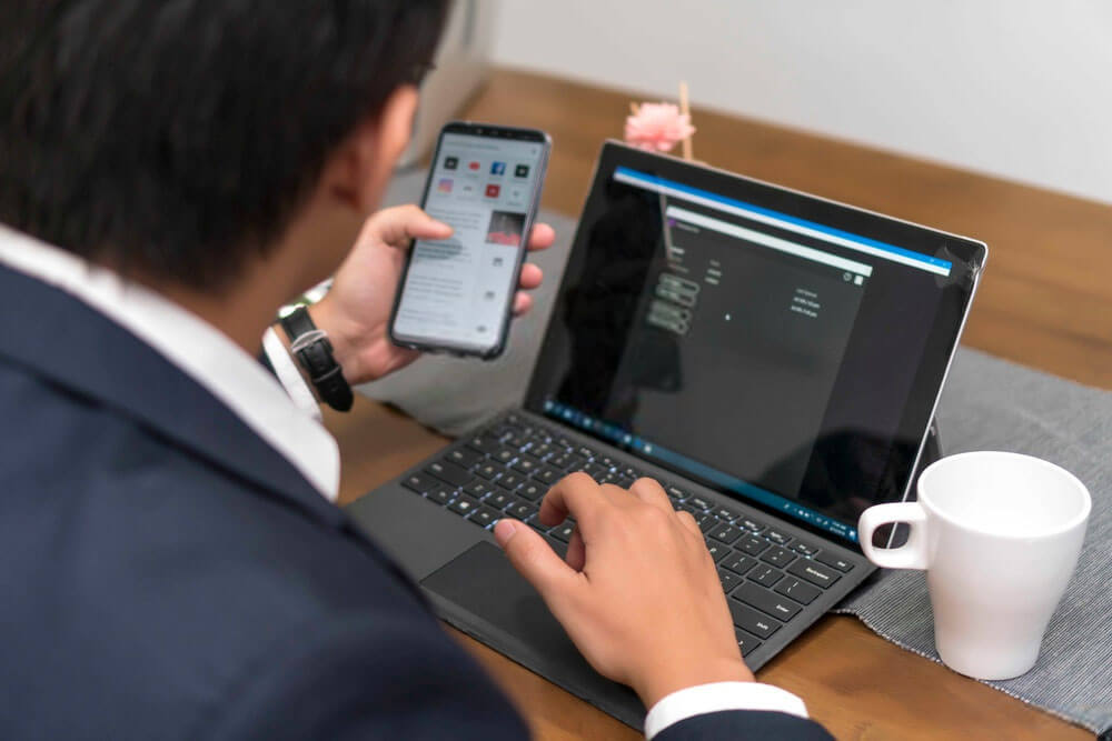 man working on laptop and holding smartphone